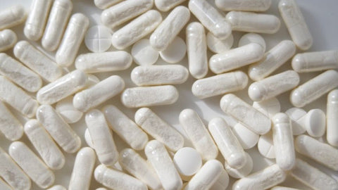 Gélules blanches de complément à base de glucosamine et chondroïtine posées sur fond clair
